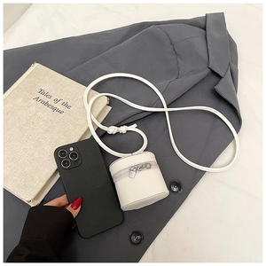 Mini white cylinder crossbody bag in lychee texture leather beside a smartphone for scale