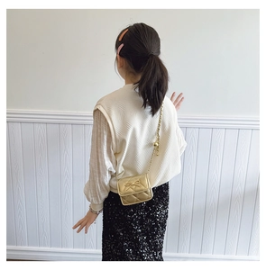 Detail of girls' golden quilted mini bag with a metallic bow and chain strap on a model