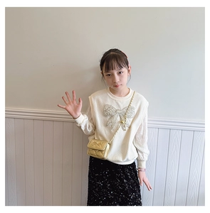 Close-up of girls cream knit sweater with sequined bow and gold quilted chain purse