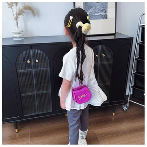 Dettaglio della mini borsa a tracolla fucsia da bambina con fiocco dorato e catenella