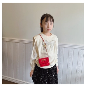 Detail of red quilted girl's crossbody bag with a golden bow and elegant chain strap