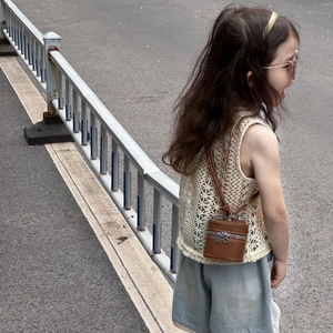 Close-up of a brown mini cylinder crossbody bag in pebble grain leather worn by a child