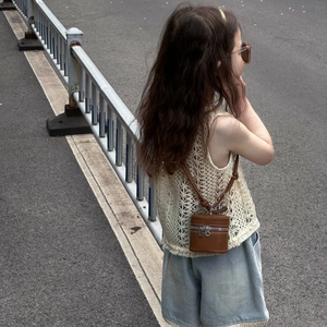 Detail of a brown leather mini bucket bag with a crochet vest and denim shorts outfit