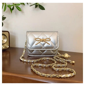 Detail of silver quilted mini bag with gold bow and metallic chain strap on wood