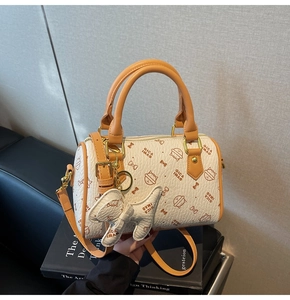 Close-up of cat print boston bag with orange handles and dog charm on black books