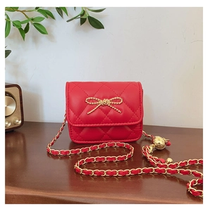 Detail of red quilted mini crossbody bag with golden bow and adjustable gold ball chain strap