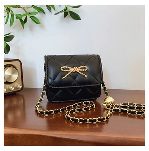 Detail of black quilted mini bag with golden bow hardware and chain strap on wooden surface