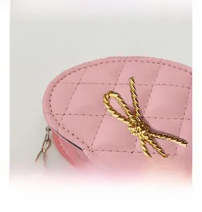 Close-up of pink heart-shaped bag with quilted texture and golden metal bow detail
