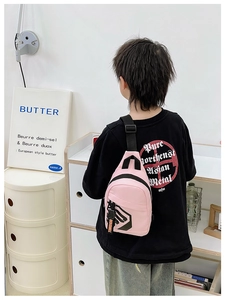 Pink kids chest bag detail with black logo and orange ribbon tag worn by child