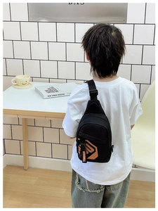 Rear view of a boy wearing a black canvas chest bag with adjustable strap and orange print