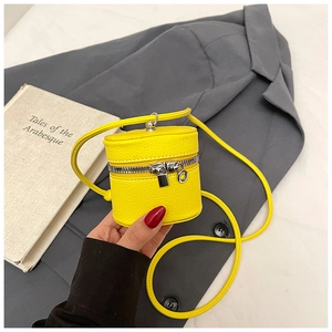 Detail of a bright yellow mini cylinder bag with litchi leather texture and silver zipper