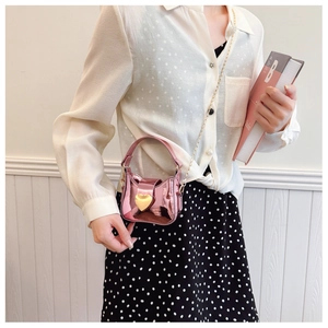 Sac à bandoulière rose métallisé avec boucle cœur dorée porté par un mannequin stylé