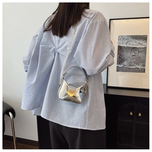 Détail du mini sac laser argenté avec serrure coeur porté par un mannequin chic