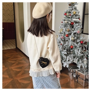Close-up of black quilted heart crossbody bag with gold bow on a festive background