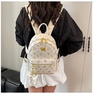 Détail d'un sac à dos blanc avec motif chat, fermeture dorée et breloque chien