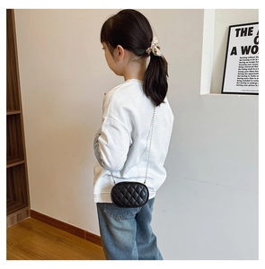 Detail of a mini quilted black oval crossbody bag for kids with silver chain strap