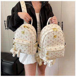 Détail du sac à dos crème avec imprimé logo, zips dorés et pendentif en forme de chiot