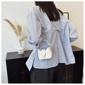 Gros plan d'un sac en cuir verni blanc avec boucle cœur dorée et bandoulière chaîne