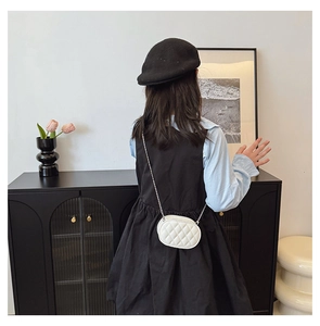 Detail of white quilted chain crossbody bag for kids shown on a young model in a home setting