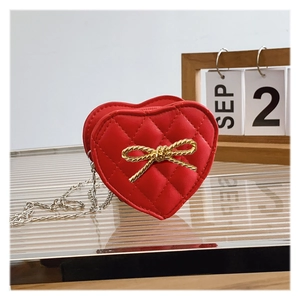Detail of red heart-shaped purse with quilted pattern and gold bow on textured glass