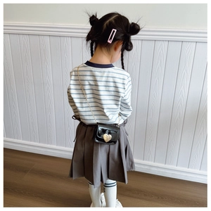 Rear view of child wearing striped top, grey pleated skirt and mini heart chain bag