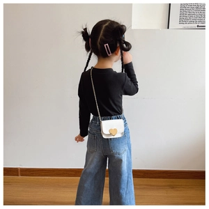 Rear view of a child wearing the white mini crossbody bag with golden heart clasp