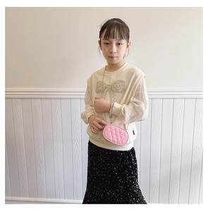 Pink quilted oval crossbody bag styled with sequined bow sweater and black skirt