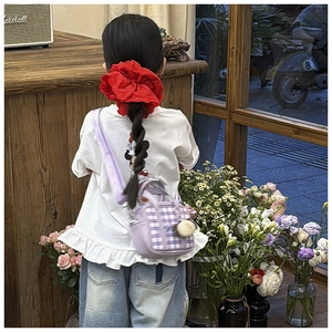 Girl wearing a purple plaid crossbody mini bag with a plush charm in a floral setting