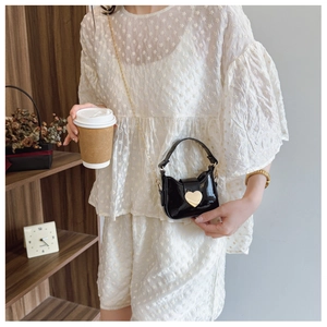 Détail d'un mini sac en cuir verni noir brillant avec boucle cœur dorée et chaîne