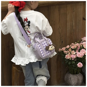 Detail of purple plaid mini kids bag with plush dog charm and adjustable strap