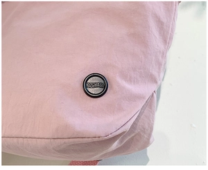 Detail of pink fabric kids bag with a round black metal TOCHASD decorative badge