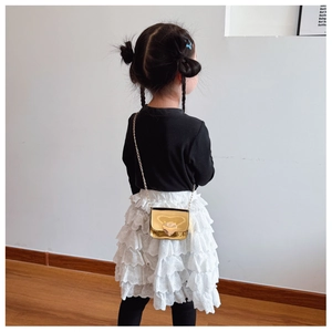 Detail of a kids black knit top and white lace skirt with a golden heart chain bag