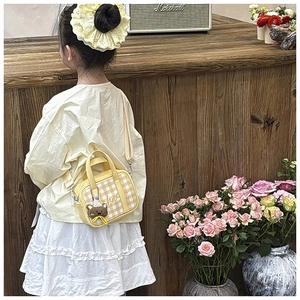 Detail of yellow checkered kids handbag with cute brown bear charm on the side