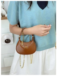 Détail d'un mini sac croissant marron avec bandoulière chaîne dorée et logo métal
