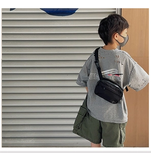 Close-up of a black canvas crossbody bag for kids styled with street fashion clothing