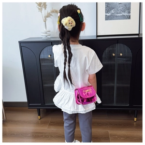 Détail d'un sac métallique rose pour enfant avec nœud doré et bandoulière chaîne sur modèle