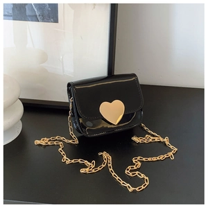 Detail of a black patent leather mini flap bag with a large golden heart lock and chain strap