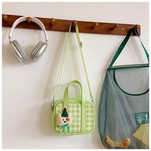 Detail of light green plaid mini handbag with bear pendant hanging on a wooden hook