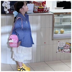 Pink checkered kids crossbody bag with white plush charm on a styled child outfit