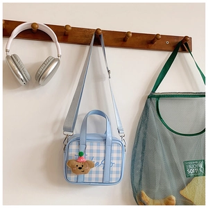 Detail of light blue checkered mini handbag with a cute plush bear charm hanging on a wooden hook