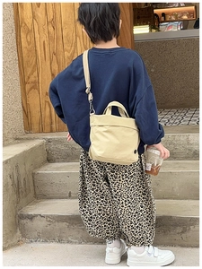 Kid's beige canvas tote bag with adjustable shoulder strap shown in a lifestyle setting