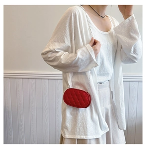 Detail of red quilted oval crossbody bag with silver chain strap on a child model