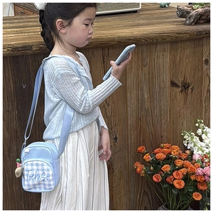 Detail of light blue plaid kids crossbody bag with small doll charm and logo print