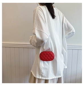 Detail of red oval quilted mini bag with silver chain strap worn by a model