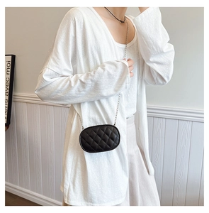 Detail of a mini black quilted crossbody bag with silver chain strap on a model
