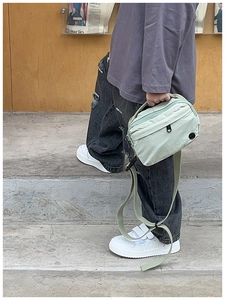 Close-up of light green canvas crossbody bag with adjustable strap and zipper detail