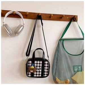 Close-up of black and white checkered kids handbag with cute plush bear charm detail