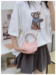 Mini sac demi-lune rose avec bandoulière chaîne dorée porté par un jeune mannequin
