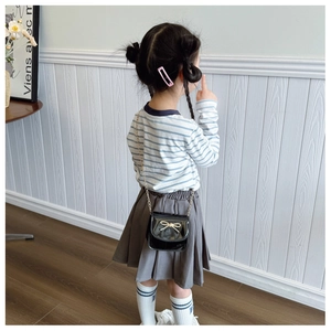 Détail d'un sac bandoulière noir en cuir verni pour fille avec un nœud doré scintillant