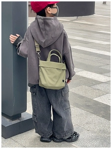 Olive green canvas crossbody bag for kids with adjustable strap in a street style shot